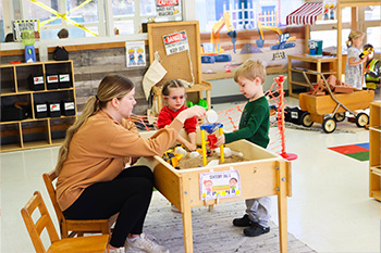 teacher works with two children at the sandbox table