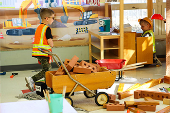 Child in a reflective safety vest pushes a cart of toy bricks
