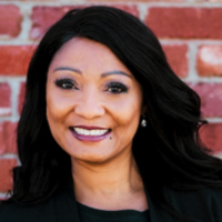 LaRonda McCarther in front of a red brick wall, smiling and wearing a black blouse.