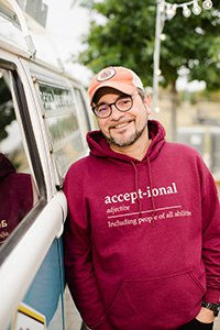 Smiling man in an orange ballcap and maroon hoodie, leaning against a van