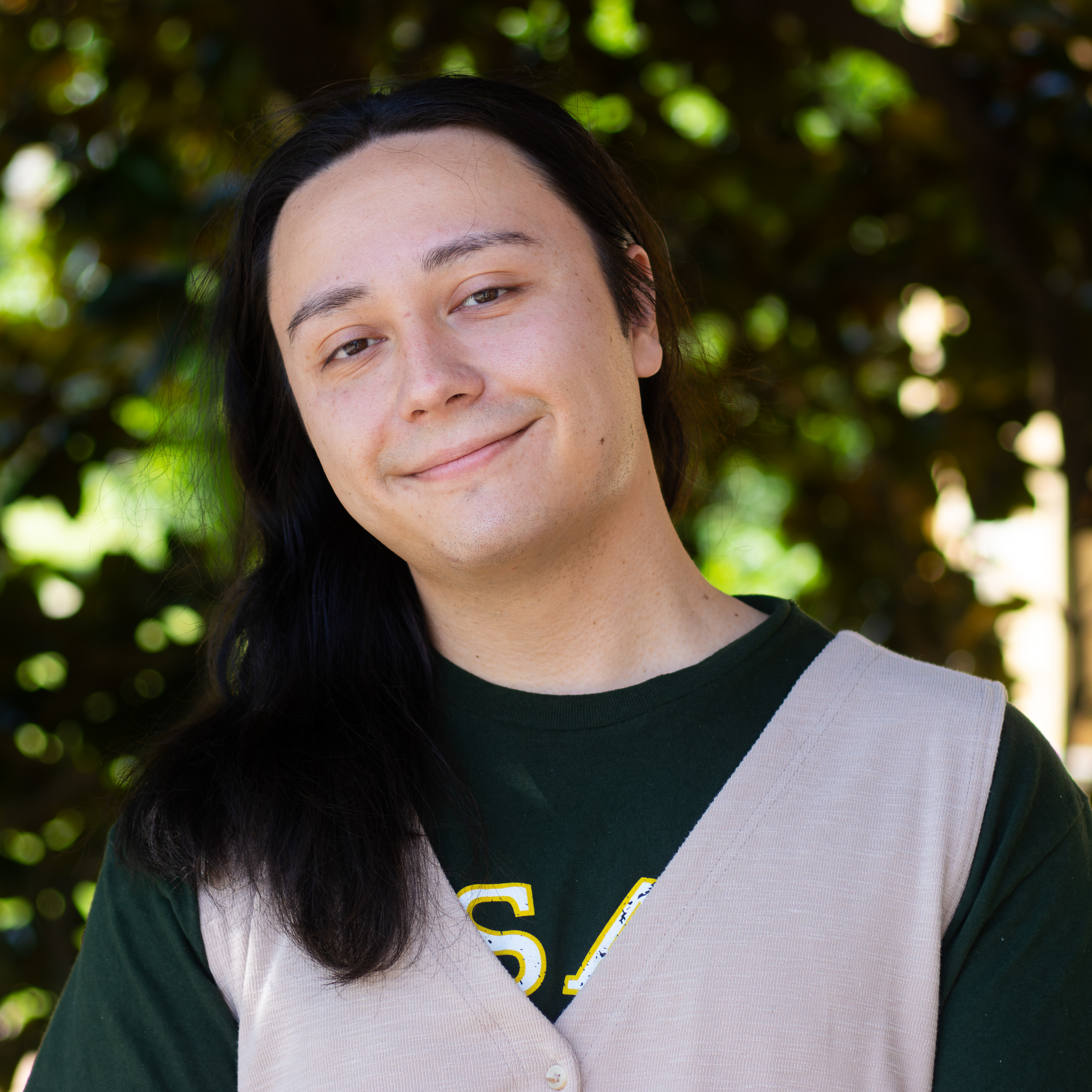 person smiling in green usao t-shirt with light gray vest and long dark hair