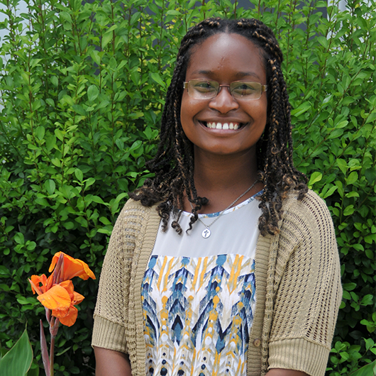 April Lawrence smiling in front of green foliage