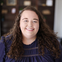 Woman with wavy brown hair wearing a dark blue shirt