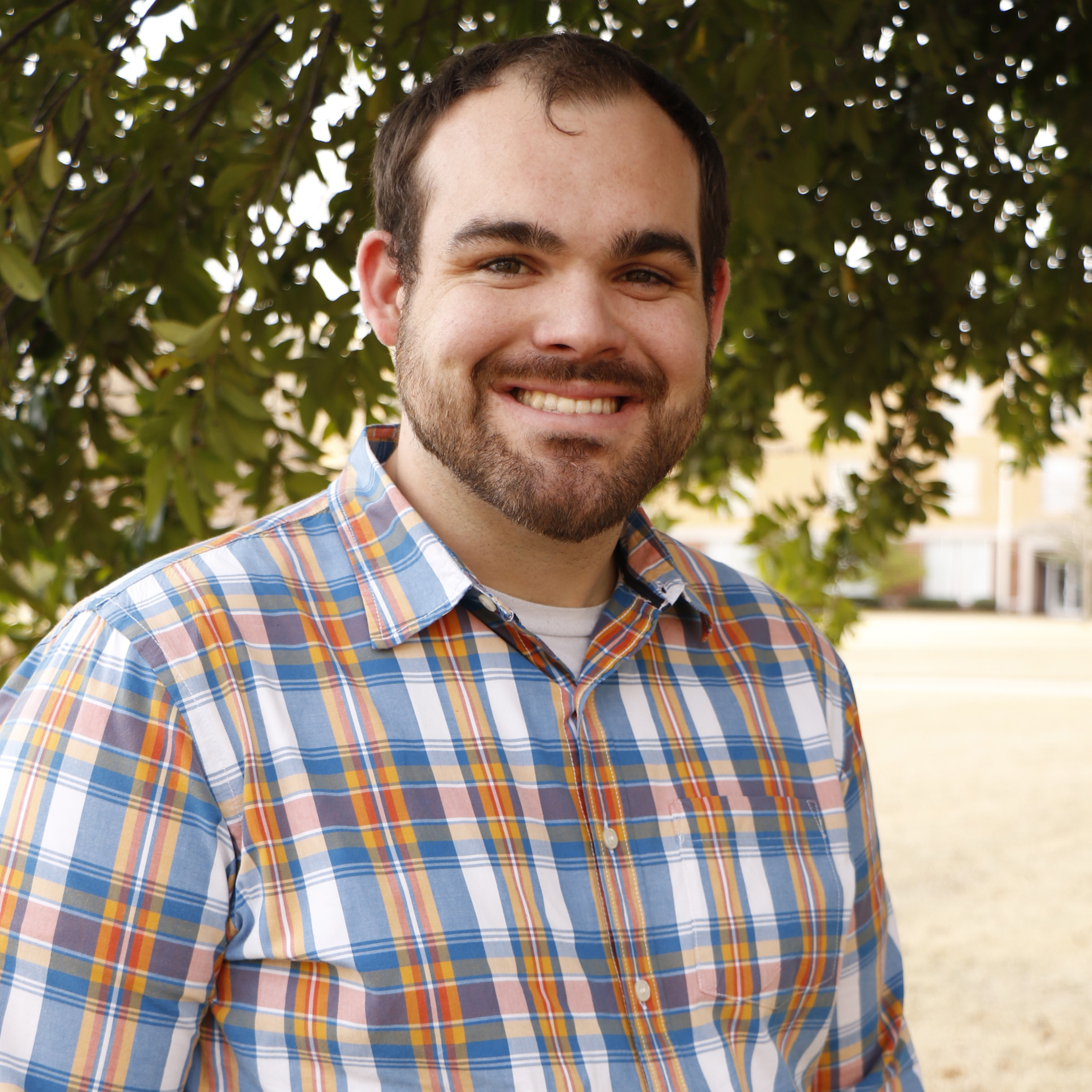 Smiling man with short beard wearing a blue and orange patterned shirt