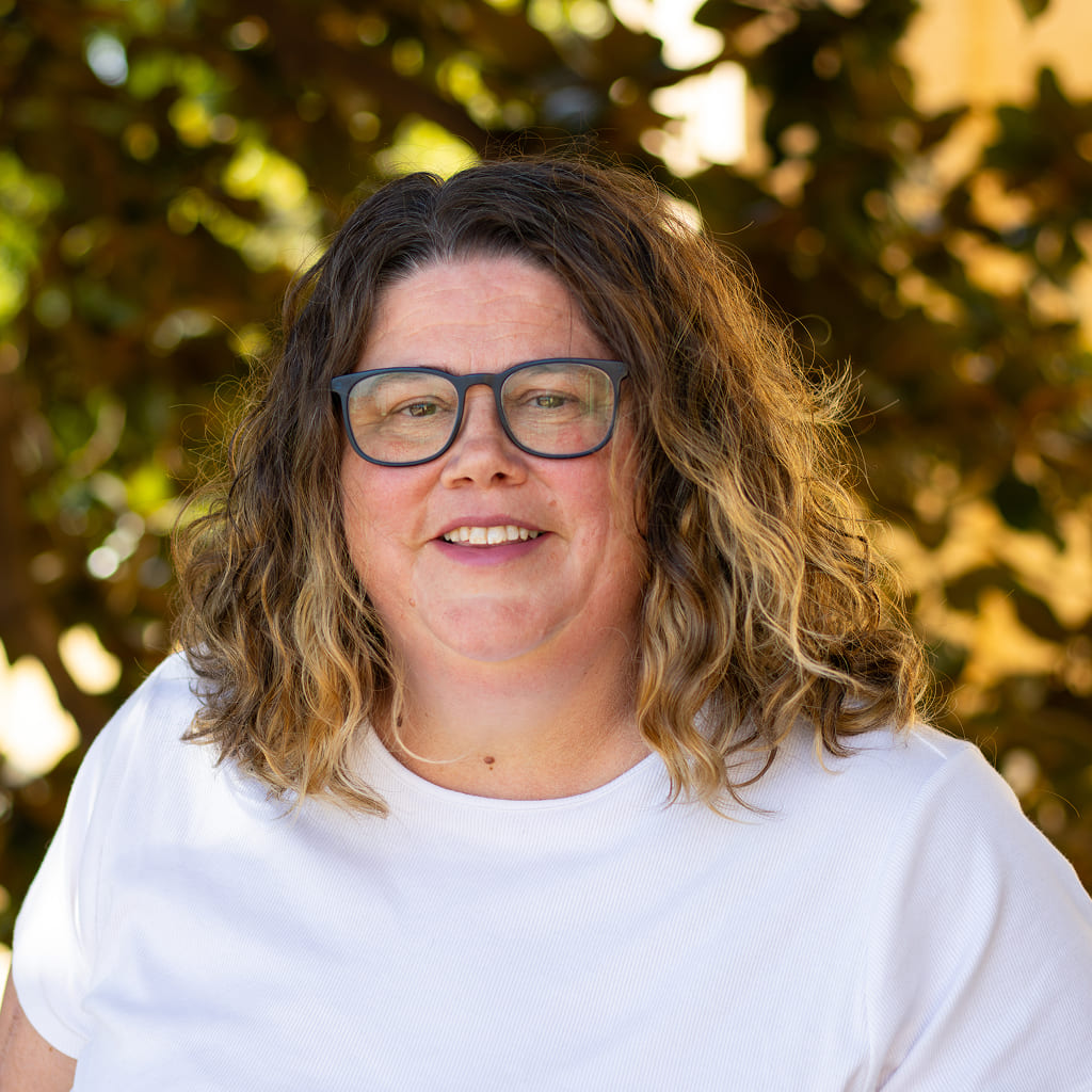A woman in white shirt and glasses standing and smiling
