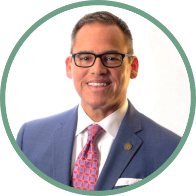 JP Audas in a navy blue suit with a red and blue tie and black rectangle glasses.