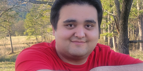 Cole Placencia standing outside wearing a red shirt and smiling.